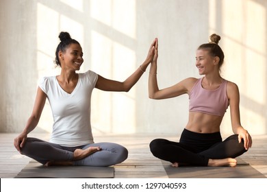 Toned smiling diverse girls sit on rubber mats give high five happy for good result practicing yoga, African American and Caucasian yogi join hands motivated for success, show unity and support - Powered by Shutterstock