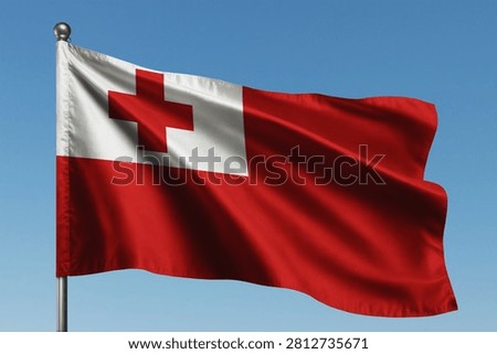 Tonga flag waving in the wind features a bold red field with a white canton containing a red cross representing the christian faith of this beautiful pacific island nation while displaying national pride under a bright and clear summer sky background.