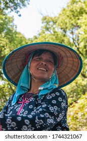 Tongli, JIangsu, China - May 3, 2010: Closeup Of Smiling Face Of Female Boat Captain Against Fade Green Foliage. Wears Blue Shirt And Towel Under Large Straw Hat.