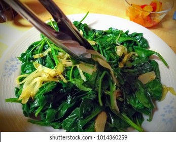 Tongs Serving Wilted Spinach And Onions. 