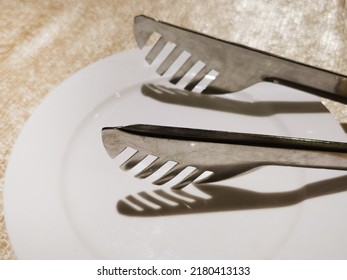 tongs are a tool for grabbing food, etc.Serving kitchen tongs on a white plate.tongs. tongs are a tool for grabbing food, etc
