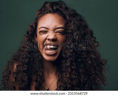 Tongue out, portrait and young woman in studio with natural curly hair, happy meme or wink on a green background. Face, crazy and female model with funny personality, goofy and silly emoji expression