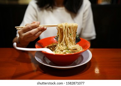 Tonkotsu Ramen - A Bowl Of Japanese Noodles Soup Made From Stock Based On Pork Bone Broth, Topped With Sliced Braised Pork (Chashu), Shredded Carrots And Spring Onions On Wooden Table.