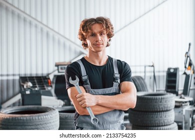 With tool in hand. Adult man in grey colored uniform works in the automobile salon. - Shutterstock ID 2133754235