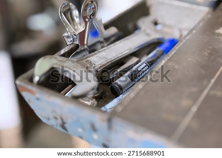 A toolbox contains various tools including wrenches and pens in a workshop setting during the day.