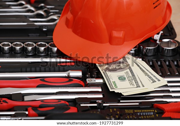 Toolbox, tools\
kit detail, dollar bills and orange protective helmet close up.\
instruments. set of tools. car tool kit. tool set background.\
instruments for repair. money for\
repairs.