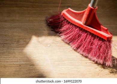 Tools For Cleaning The House. Red Sweeping Brush With Artificial Bristles And A Long Handle On The Background Of The Vinyl Floor Covering In The Kitchen, Imitated By Oak, Close-up