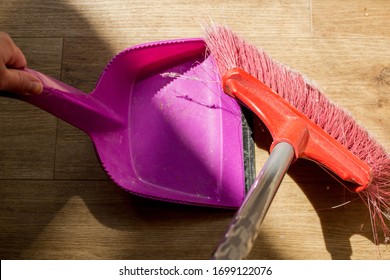 Tools For Cleaning The House. A Red Sweeping Brush With Artificial Bristles  And A Purple Dustpan Against The Background Of The Vinyl Floor Covering In The Kitchen Close Up During Cleaning