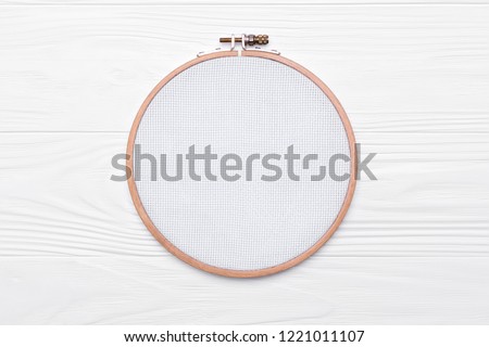Tools for cross stitch. A hoop for embroidery and canvas on white wooden background. Mockup for hobby