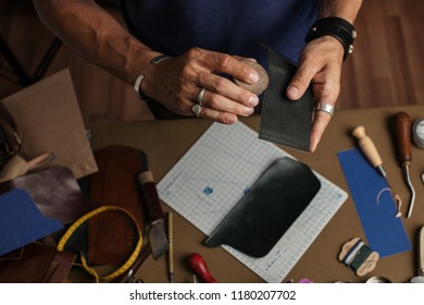 Tools and equipment for leather handmade goods. Cropped image of a male artisan making custom made wallet design for a new client at his workshop. Leathercraft, Small business, Handwork Concept.