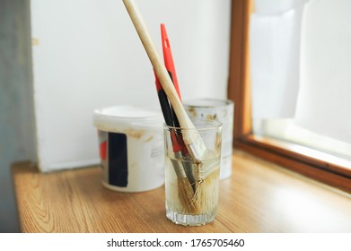 tools for home self-repair. wall paint brushes soaked in water, blurred cans of paint on the background stand on a wooden window in the room - Powered by Shutterstock