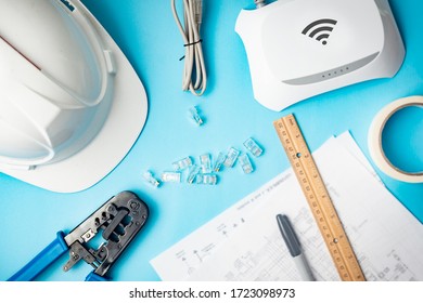Tools for installation of wireless networks and structured cabling. Engineer helmet, network cable, ruler, blades, frames, modem, utp terminals on blue background.