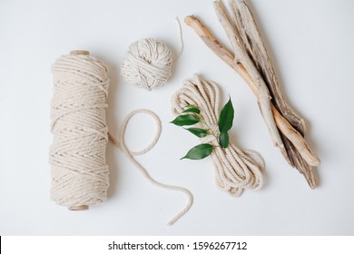 Tools and materials for macrame weaving over white surface. Cotton ropes and sticks from the river, grinded by water. Flat lay, top view.