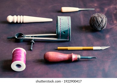 Tools for processing and creating leather products are laid out on the desktop in the leather workshop. In the center there is a blank of a leather product