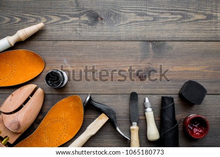 Tools for shoe repair. Hummer, awl, knife, sciccors, wooden shoe, insole, paint and leather. Dark wooden background top view copy space
