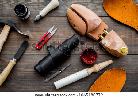 Tools for shoe repair. Hummer, awl, knife, sciccors, wooden shoe, insole, paint and leather. Dark wooden background top view pattern