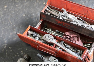 Tools In Steel Box. Red Open Tool Box On Dirty Garage Floor.