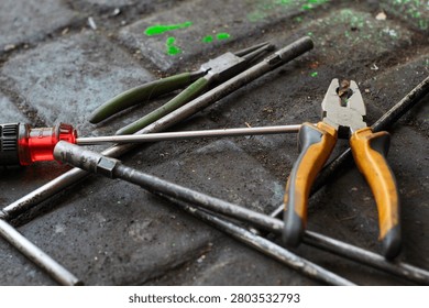 Tools such as pliers, screwdrivers, and socket wrenches are placed haphazardly on the dirty, textured workshop floor.