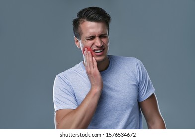 Tooth ache concept. Indoor shot of young male feeling pain, holding his cheek with hand, suffering from bad toothache, looking at camera with painful expression - Shutterstock ID 1576534672