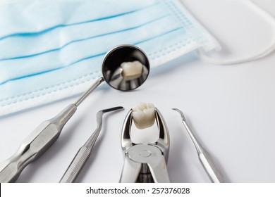 Tooth extraction concept with an array of stainless steel dental tools and a mask with the extracted tooth clasped in the pincers and reflected in the mirror