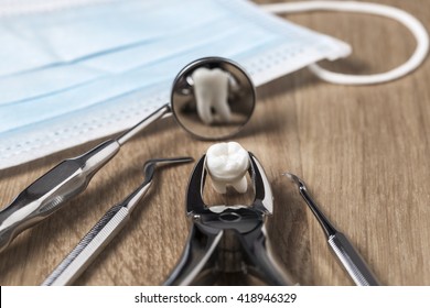 Tooth extraction concept with an array of stainless steel dental tools and a mask with the extracted tooth clasped in the pincers and reflected in the mirror