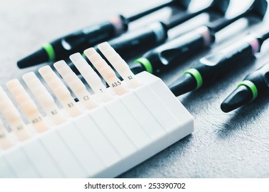 Tooth Shade And Color Guide On The Table With Dental Filling Injection Tubes Behind