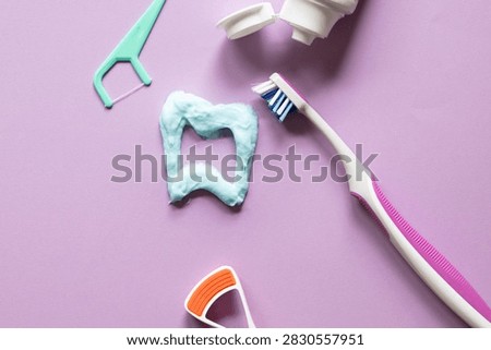 Tooth shape drawn with toothpaste on purple background with dental hygiene tools, toothbrush, tongue scraper, and dental floss.