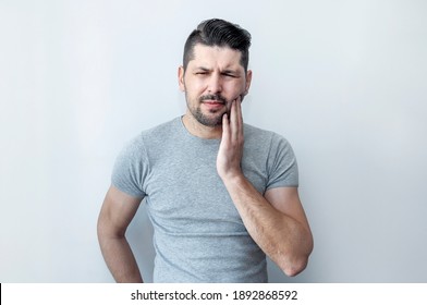 Toothache concept. Frustrated young man touching his cheek suffering terrible strong teeth pain. 