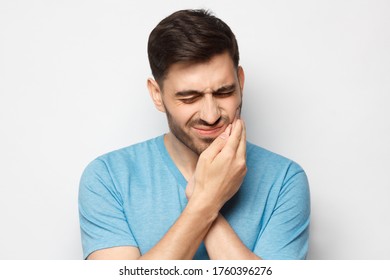 Toothache concept. Young man feeling pain, holding his cheek with hand, suffering with painful expression, isolated ion gray background