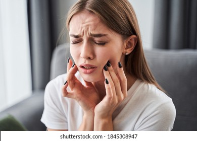 Toothache. Girl Suffering From Tooth Pain And Touching Cheek While Sitting On Couch At Home. Dental Problem Concept. Stock Photo