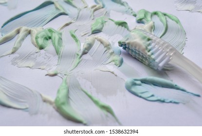 The Toothbrush Is All Smeared With Toothpaste, Lying Among Smears Of Paste Green, Blue And White On A White Background. The Concept Of Freshness, Oral Hygiene, Teeth Cleaning