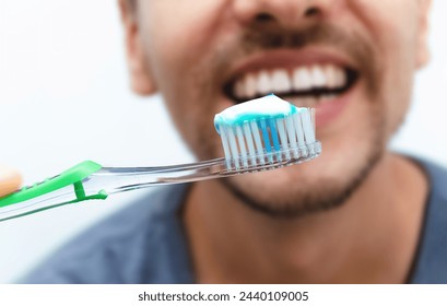 Toothbrush with toothpaste in close-up with smile of young man behind. Oral hygiene. World Oral Health Day. Cleaning and brushing teeth with fluoride.