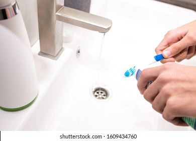 Toothbrush with toothpaste in the guy's hand on the background of the washbasin. - Shutterstock ID 1609434760