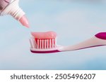 Toothbrush with toothpaste on blue background. Applying toothpaste on brush against blurred background. Means to care for the oral cavity.