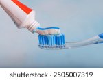 Toothbrush and toothpaste, Squeezing toothpaste onto toothbrush. Applying toothpaste on brush against blurred background, closeup.