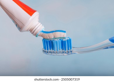 Toothbrush and toothpaste, Squeezing toothpaste onto toothbrush. Applying toothpaste on brush against blurred background, closeup.