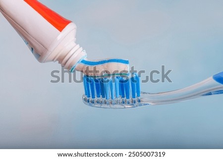 Toothbrush and toothpaste, Squeezing toothpaste onto toothbrush. Applying toothpaste on brush against blurred background, closeup.