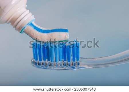 Toothbrush and toothpaste, Squeezing toothpaste onto toothbrush. Applying toothpaste on brush against blurred background, closeup.