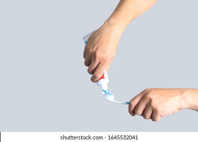 Toothbrush And Tube Of Toothpaste In A Hand Isolated On Gray Background, Squeezing Toothpaste On The Toothbrush