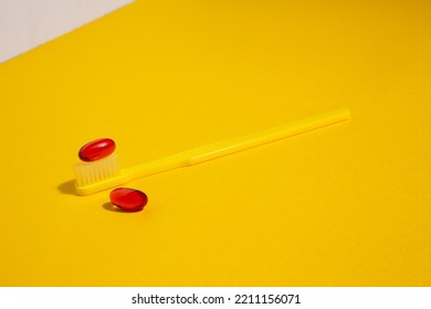 A Toothbrush And Two Red Soft Gel Capsule Pills Isolated On Yellow Background With Copy Space