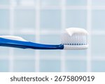 Toothbrush with white toothpaste close up on blue tile background.