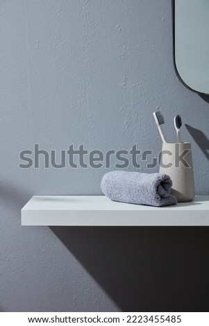 Toothbrushes in cup and towels on a white table inside bathroom with a cement wall. Minimal decoration.
Morning Sunlight, Product display background, Mock up.