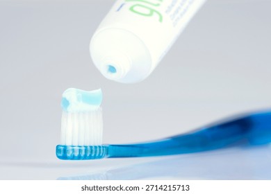 Toothpaste being applied to a blue toothbrush in a well-lit setting for daily oral hygiene routine