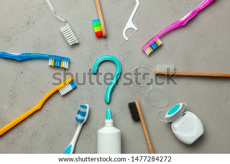 Toothpaste in the form of a question mark and many different and colored toothbrushes and dental floss. Concept of how to choose the right toothbrush or how to brush your teeth.