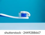 Toothpaste on a toothbrush close-up on a cyan-white background 