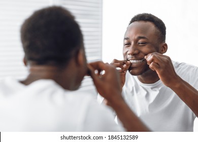 Toothy African Man Flossing And Cleaning Teeth Using Tooth Floss Standing Near Mirror In Modern Bathroom At Home In The Morning. Toothcare And Healthy Oral Hygiene Concept. Selective Focus - Powered by Shutterstock