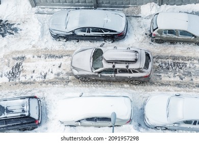 Top Above Aerial View Of Modern Suv Crossover Car With Roof Rack Box Trunk Driving Through Vehicles Parked On City Street Covered By Deep Snow On Clod Frosty Winter Day. Apartment Building Driveway