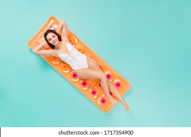 Top above high angle full length photo positive peaceful girl have holiday trip resort swim lay float rubber air bed close eyes enjoy wear white bodysuit isolated over teal color background