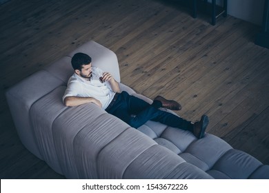 Top above high angle view of his he nice attractive serious imposing guy lying on divan drinking beverage having rest free spare time at modern industrial loft interior open space work place station