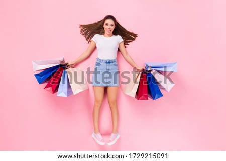 Top above high angle view full size photo of childish playful girl lay have shopping rest hold bags show tongue out wear white t-shirt isolated over pastel color background
